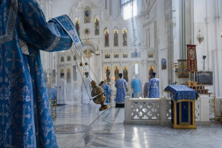 Priester met zwaaiend wierookvat tijdens een dienst in een lichte orthodoxe kerk.