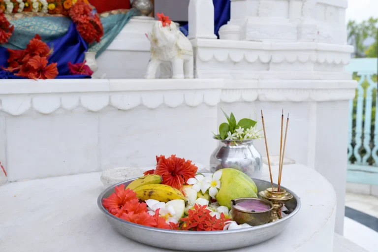Schaal met bloemen, fruit en wierookstokjes voor een wit tempelaltaar tijdens een puja.