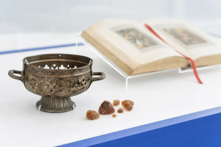 Antieke metalen wierookschaal met harskorrels voor een open boek in een lichte museumopstelling.